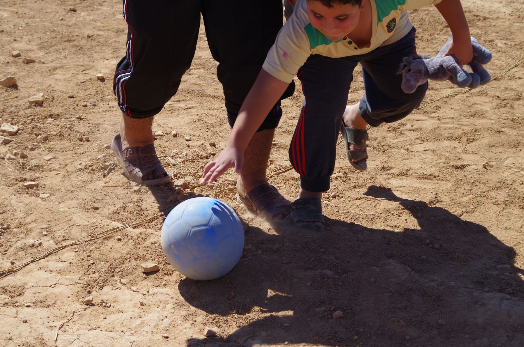 Close up of a child's foot meeting a blue ball on dusty ground