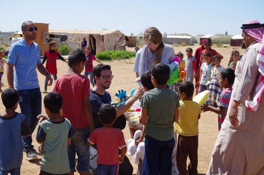 Aid workers hand out toys to a crowd of children in a camp